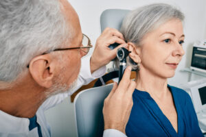 A doctor using an otoscope to look at an older woman's ear.
