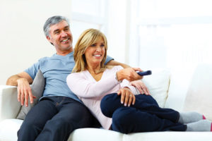Happy middle-aged couple watching TV. Woman is adjusting the volume