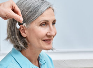 Installation hearing aid on senior womans ear at audiology center, close-up, side view. Deafness treatment, hearing solutions